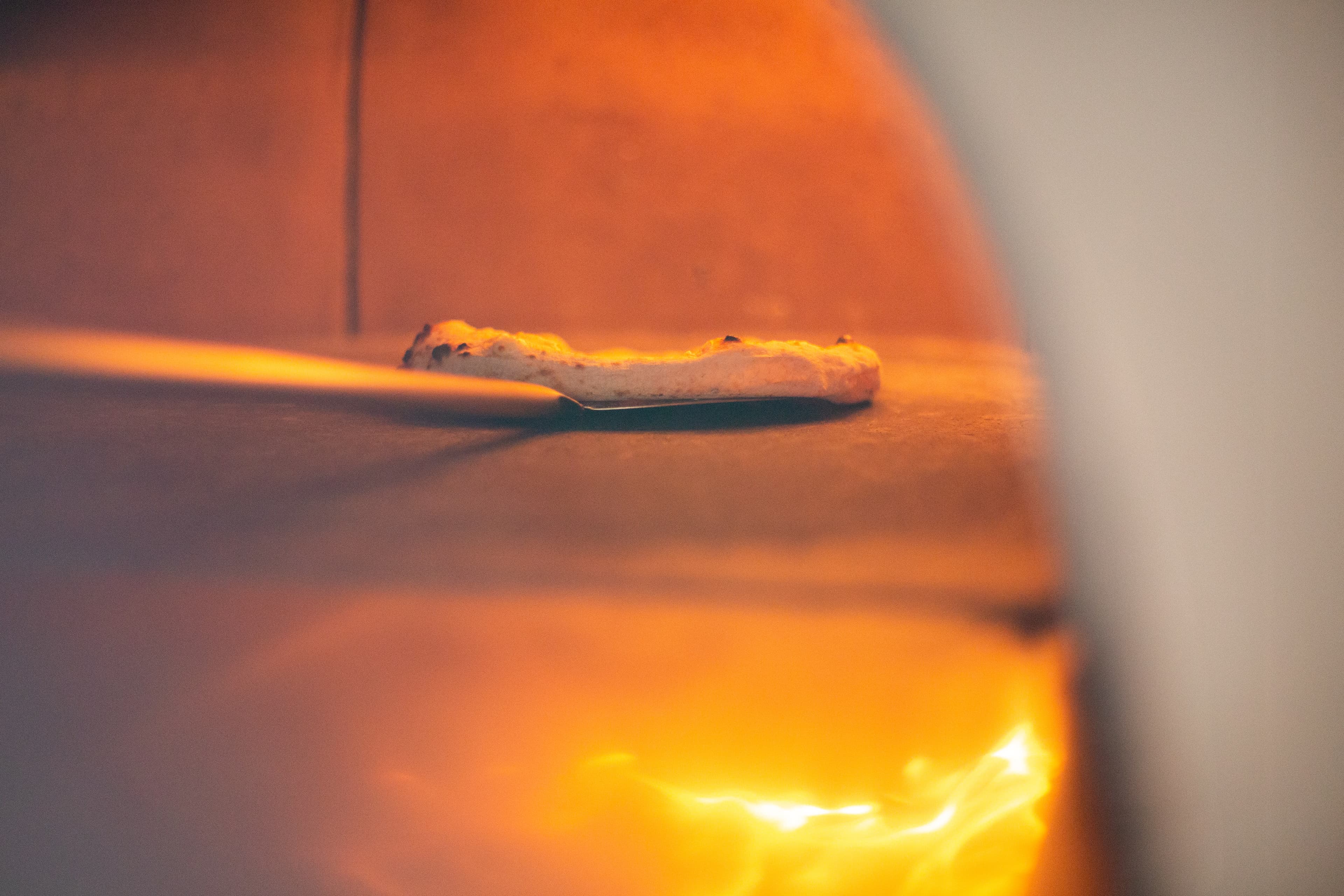 Pizza en cuisson dans un four professionnel, vue rasante sole et flammes